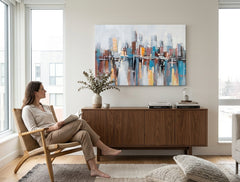 Tabloul cu peisaj urban abstract, în tonuri de albastru, maro și galben, este agățat într-un interior modern, deasupra unei console din lemn cu o vază și o lumânare, Papilora.