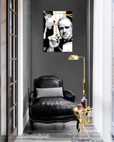 Tabloul cu portretul lui Don Corleone, în alb și negru cu detalii aurii, este agățat într-un interior modern și elegant, deasupra unei console din lemn cu o vază și o lumânare, Papilora.