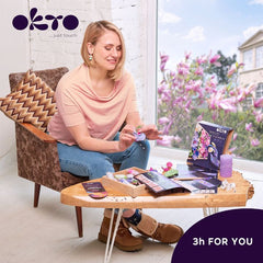Un aranjament floral 3D plin de culoare, cu nuanțe de roz și violet, este expus într-un interior modern, deasupra unei console din lemn cu o vază și o lumânare, Papilora.