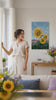 Tablou cu trei floarea-soarelui pe câmp – cu detalii pictate manual. Tablou premium pictat cu acrilic, decor modern de perete pentru sufragerie, o femeie admiră opera într-un interior stilat luminos. Papilora Premium Art (XOGAI018E1).